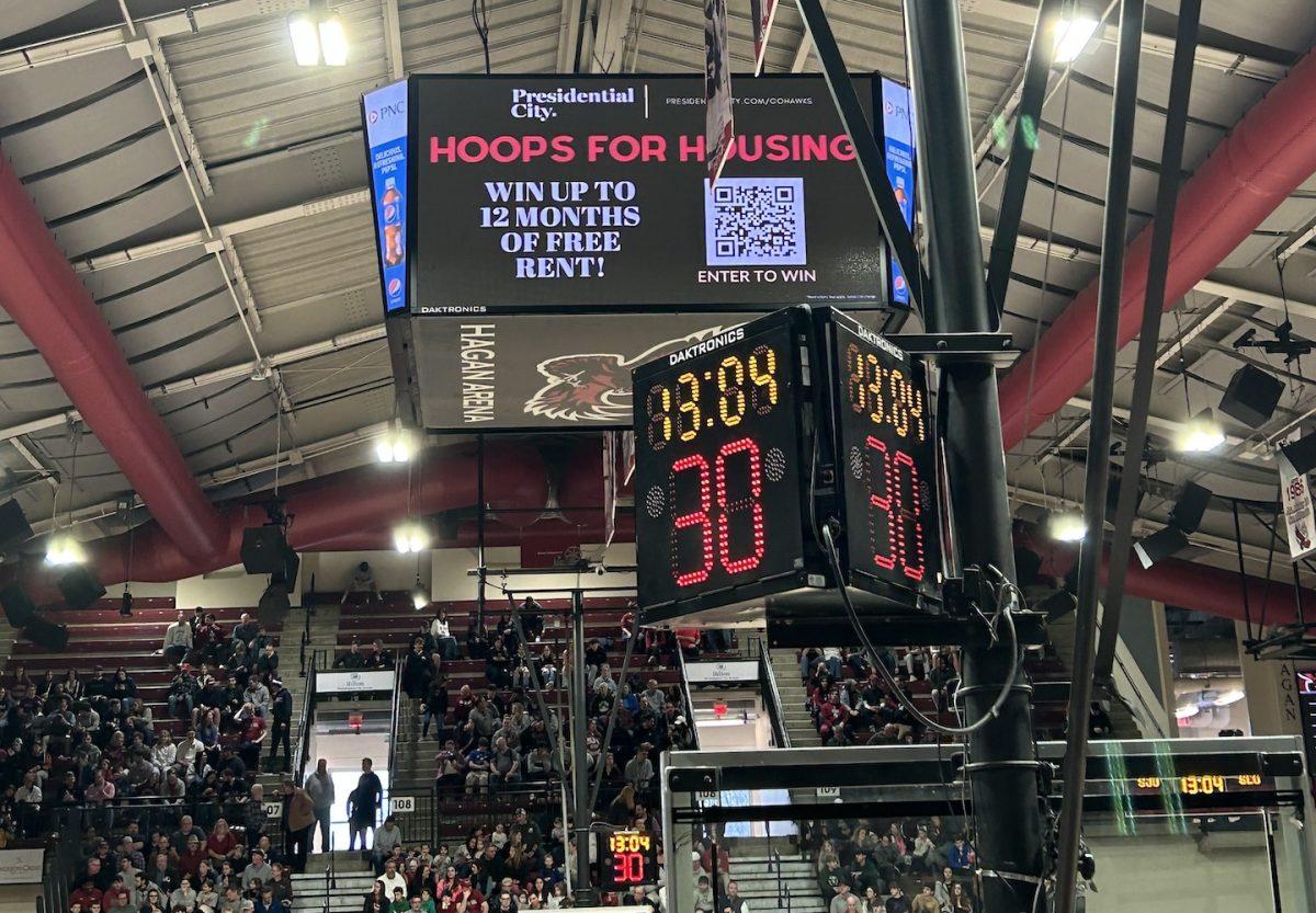 Photo of the jumbotron at displaying the Hoops for Housing halftime free throw contest in Hagan Arena, with fans in the background