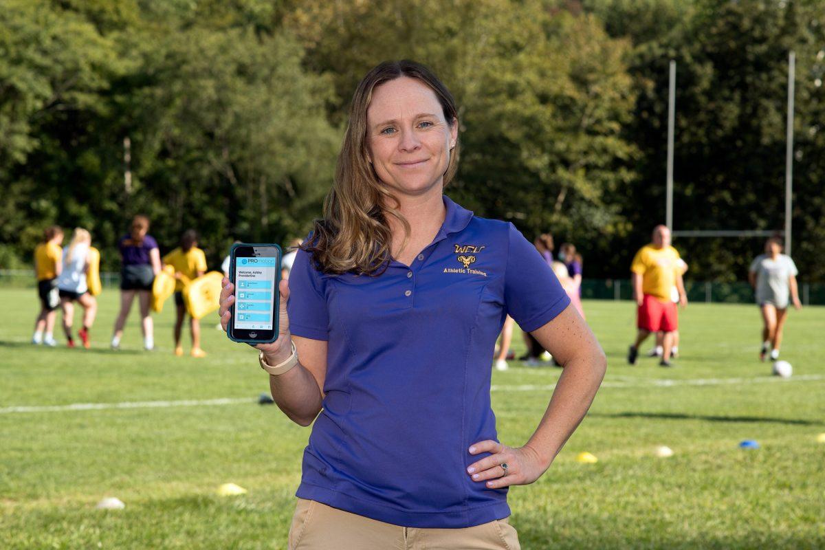 Photo of Lindsey Keenan holding phone to the camera with PROmotion app visible, rugby game in background