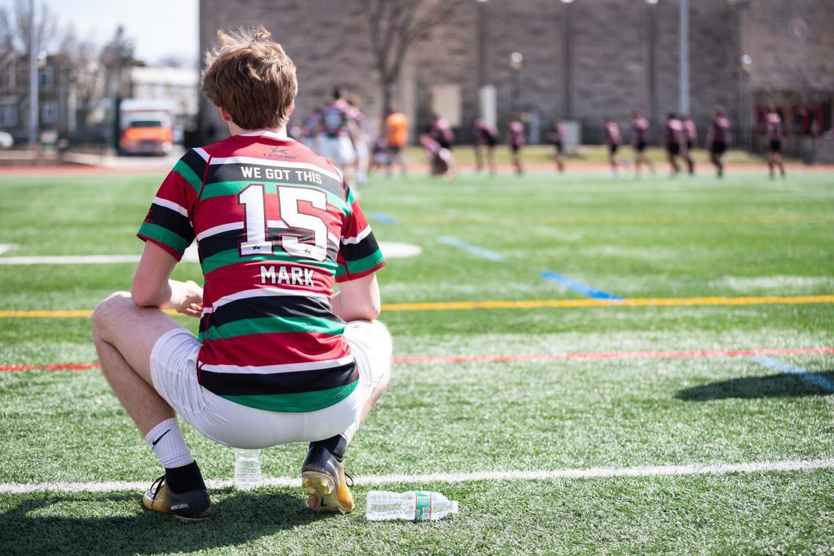 An Archmere Auks player watches his teammates play, donning a jersey commemerating Mark Dombroski 21. PHOTO: MITCHELL SHIELDS 22/THE HAWK