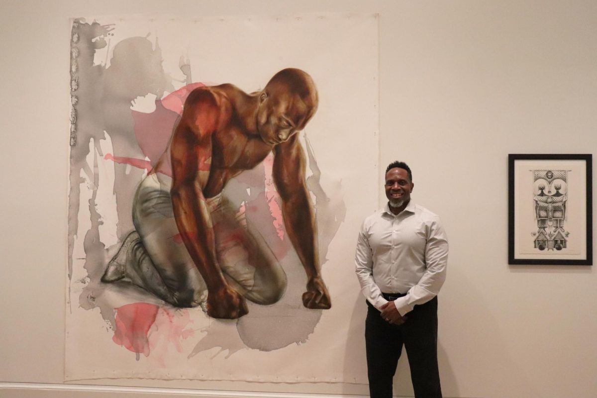 Artist Imo Nse Imeh poses in front of his painting, “Feeding the Veins of the Earth (Grounded Angel),” Sept. 29. PHOTO: ZACH PODOLNICK ’26/THE HAWK