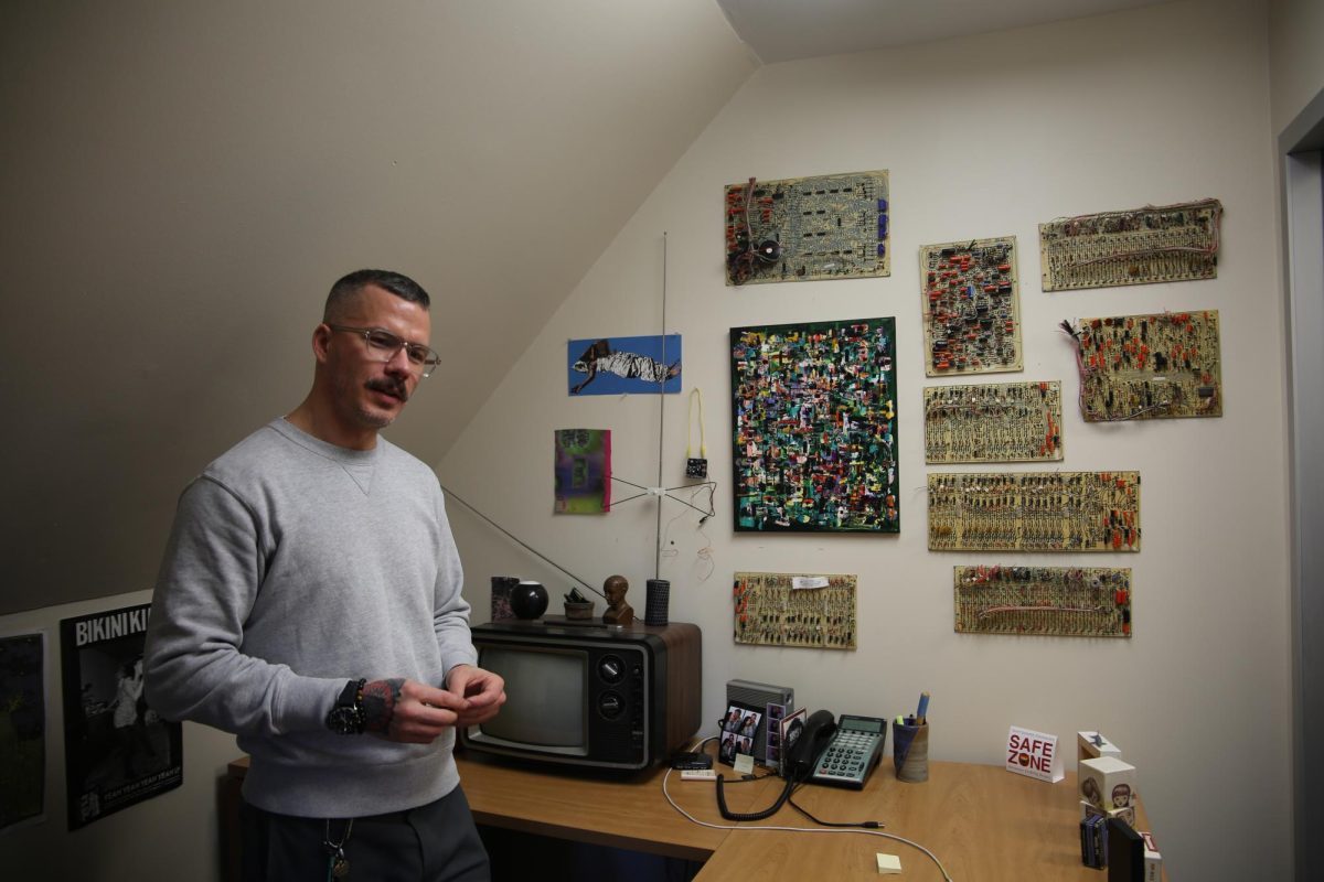 Steven Hammer, Ph.D., associate professor of communication and media studies, explains his wall of circuit boards he has collected over the years.