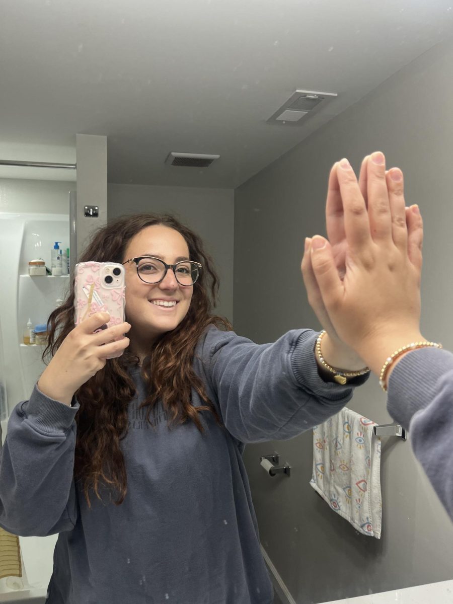 Mia Messina ’25 high fives herself in the mirror as part of the Mel Robbins morning routine. PHOTO: MIA MESSINA ’25/THE HAWK.