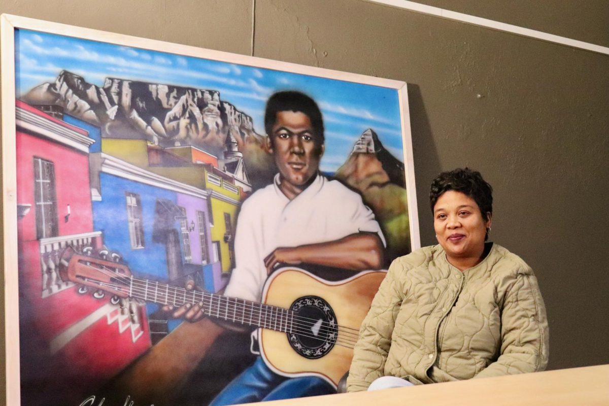 Lorreal De Lange, founder of ELDOS-FM, sits in the front of a portrait of Johnathan Butler, a South African guitarist and singer-songwriter whose music is frequently played on the station. PHOTO: FINNEGAN CROWLEY/THE HAWK