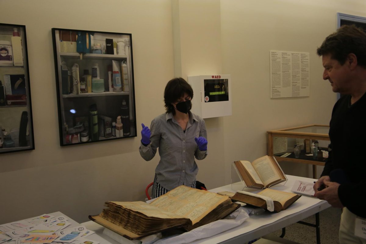 Emma Gunuey-Marrs, assistant museum curator of the Marvin Samson Museum for the History of Pharmacy, sits behind a display of relics from the St. Joe’s College of Pharmacy Museum Collection. PHOTO: ZACH PODOLNICK ’26/THE HAWK